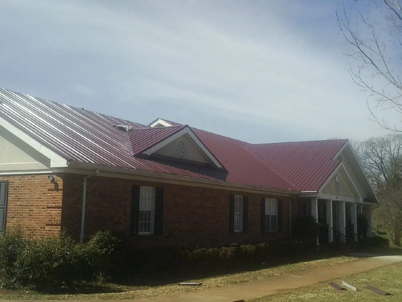 Red metal roof with gabled entries on a long brick building, from a Hail Damage Roof Repair job in Winterthur